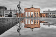 Brandenburg gate after the rain, beautiful reflection of the yellow golden gate in the water of a street puddle, grey sky with clouds in the background