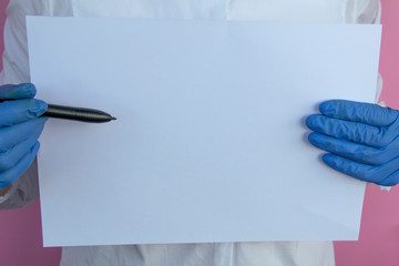 Female doctor in blue latex gloves holds a white sheet of paper and a pen.