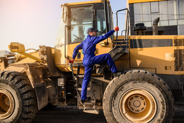 Young man contractor builder climbs into the bulldozer cabin