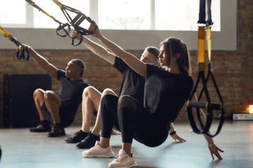 Wall Mural - Power Performance. Full-length shot of men and women doing fitness TRX training exercises at industrial gym. Push-up, group workout concept