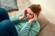 © Svitlana - Young frustrated woman sitting on the couch at home with closed eyes and suffering from headache or migraine, holding head with hands