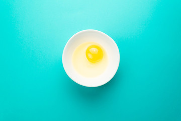 Raw egg in bowl on blue background. Healthy food and cooking at home concept.