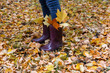 © September - Girl walking in autumn park in rubber boots with yellow leaves in her shoes