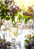 Fototapeta Nowy Jork - Refreshing cold yellow lemonade in a transparent cup and lilac in a vase are on the table