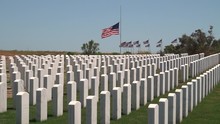 American Flags Fly Behind White Grave Markers In A Military Cemetery