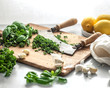 © The Picture Pantry - A knife with two handles resting in a pile of minced, green herbs on a wood cutting board, surrounded by lemons, cloves of garlic, and a white napkin