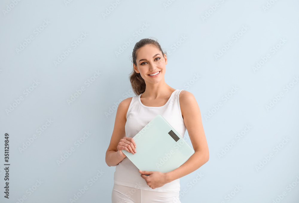 Young woman with weight scales on color background