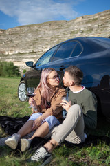 Young and beautiful couple, drinking wine in nature near the car