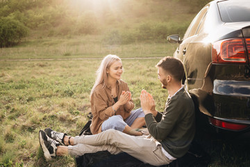 Beautiful young couple having fun at sunset near car