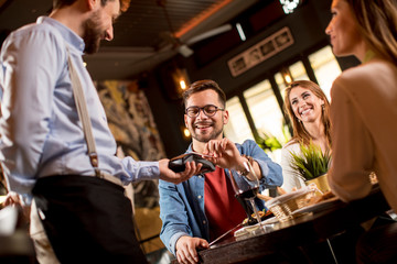 Young man paying with contactless credit card in restaurant after dinner