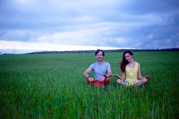 Romantic couple in relationship, sitting, kissing and hugging in the countryside field of green grass in overcast sky . Young happy girl dressed maxi dress enjoy the freedom of the meadow