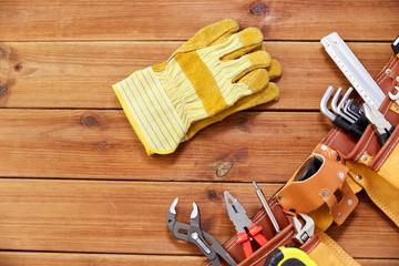 repair, building and renovation concept - gloves and belt with different work tools in pockets on wooden boards background