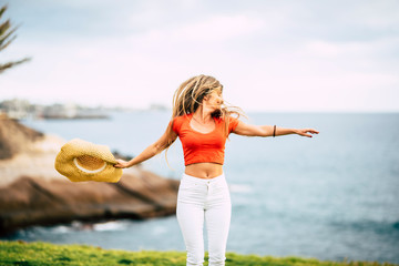 Wall Mural - Happiness and joyful freedom people concept - young beautiful slim woman with long hair jump and dance in outdoor leisure activity alone with ocean and nature green meadow background