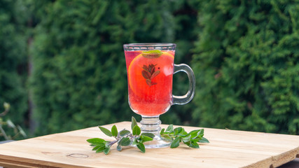 Wall Mural - glass goblet with cold cocktail on a wooden table in the garden on a background of green plants