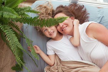 happy and beautiful mother and little daughter lie on a blue sofa near the window, a batman and a ch