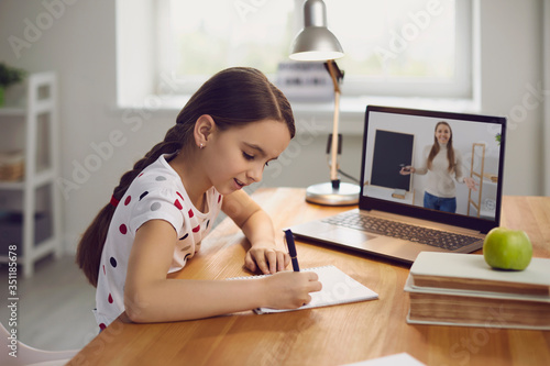 Online training. The teacher teaches the child a video call chat classroom video conferencing. Little girl teach a lesson using a laptop with sitting at a table at home.