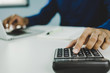 © Vittaya_25 - businessman in blue shirt hand calculate about financial with calculator and working on laptop computer and report on desk at home office, digital marketing, business finance, accountant concept