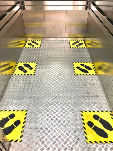 Social distancing for COVID-19 coronavirus crisis prevention with yellow footprint sign on elevator floor with text caution to respect social distance in public lift area