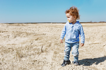 A little girl at the age of 2 walks along the sandy desert in jeans and a white T-shirt. Clear sunny day.