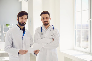 Wall Mural - Two practicing doctors with clipboard standing in a clinic office.