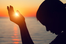Silhouette Of Young Woman Raising Hands Praying At Sunset Or Sunrise Light, Yoga Practice, Religion, Freedom And Spirituality Concept
