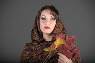 beautiful Russian brunette woman with a scarf on her head and autumn leaves in her hands