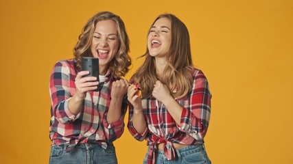 Sticker - Young concentrated girls isolated over yellow wall background using mobile phone holding credit card