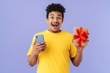 Poster - Photo of astonished african american man holding gift box and cellphone