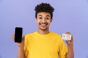 Wall Mural - Photo of smiling african american man showing credit card and cellphone