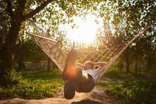 Blurry And Defocus Relaxing In Hammock In Sunny Day. Man Rest In Garden. Summer Vibes In Green Forest