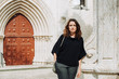 © Olga - Young Caucasian woman standing at portal of a gothic church wearing dark casual clothing and looking at camera. Lisbon as a travel destination concept. Architecture elements, entrance group context