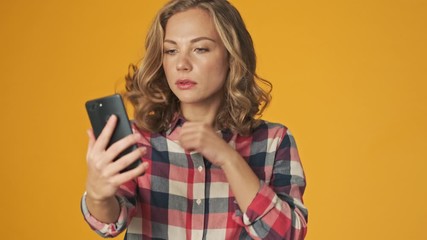 Wall Mural - Young girl isolated over yellow wall background take a selfie looking at phone as in a mirror