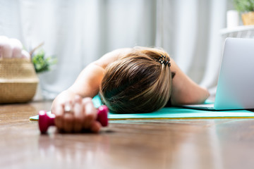 Woman falling asleep. Tired after exercise and workout. Overtraining concept. Exhausted woman lying on floor and resting after heavy cardio training in home gym at yoga mat.