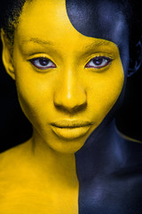 Wall Mural - Woman with black body paint. Cheerful young african girl with art bodypaint. An amazing model with yellow makeup. Closeup face.