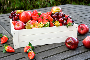 White box with variety of fresh organic fruits on wooden garden table.