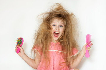 Wall Mural - a little girl with tangled long hair in a pink dress on a white background. stands with two combs in