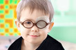 A little boy wearing glasses and an eye patch (plaster, occluder) undergoes a hardware vision treatment to prevent amblyopia and strabismus (squint, lazy eye). Child congenital vision disease problem.