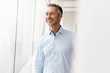 © Westend61 - Smiling mature businessman in office looking out of window in office