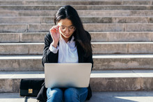Young Businesswoman Sitting On Stairs Outdoors Using Laptop