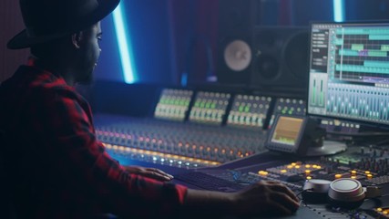 Poster - Male Audio Engineer, Producer Working in Music Recording Studio, Uses Mixing Board and Software to Create Hit Track. Portrat of Black Artist Musician Using Control Desk to Produce New Track. Side View