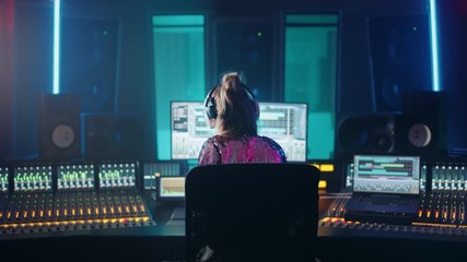 Wall Mural - Artist, Musician, Audio Engineer, Producer in Music Record Studio, Uses Control Desk with Computer Screen showing Software UI with Song Playing. Celebrates Success with Raised Hands, Dances. Back View