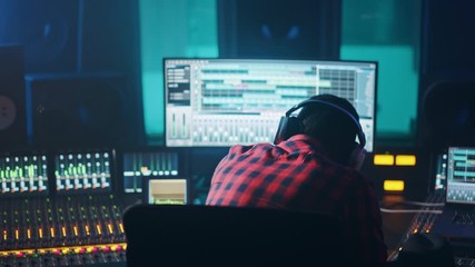 Poster - Stylish Artist, Musician, Audio Engineer, Producer Takes Place at His Control Desk in Music Record Studio, Uses Computer Screen show User Interface of DAW Software with Song Playing. Back View