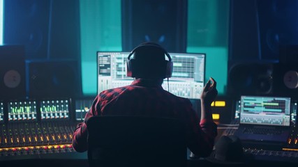 Fototapete - Artist, Musician, Audio Engineer, Producer in Music Record Studio, Uses Control Desk with Computer Screen showing Software UI with Song Playing. Success with Raised Hands, Dances. Back View. Zoom out