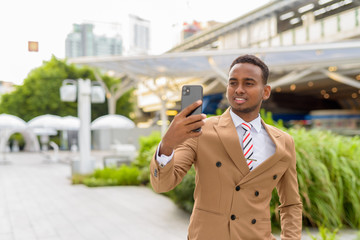 Wall Mural - Happy young handsome African businessman taking selfie in the city