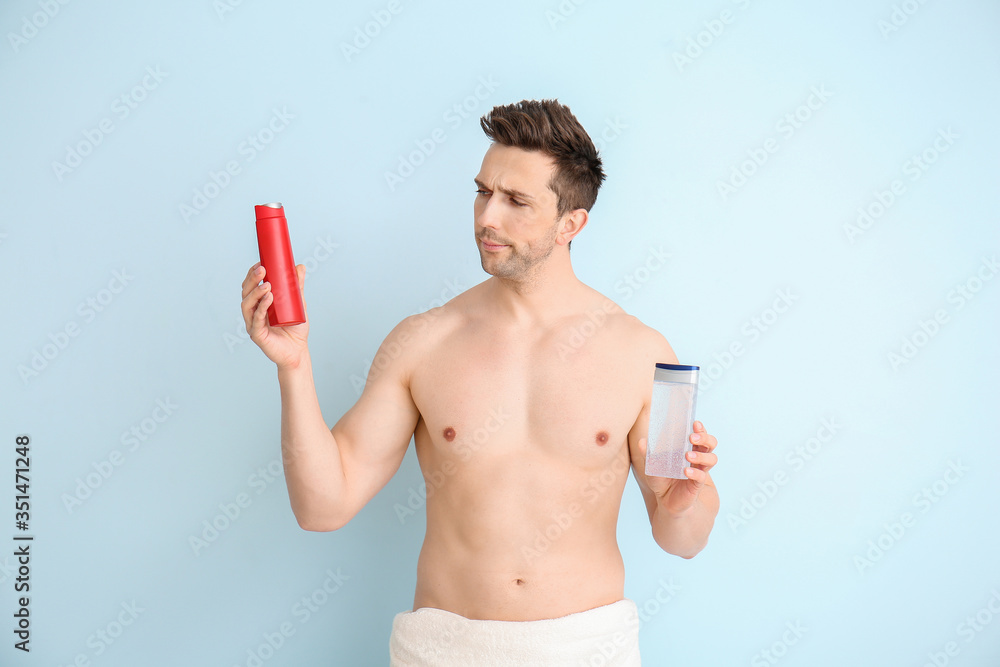 Handsome man with shower gels on color background