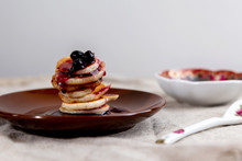 A Stack Of Mini Pancakes On A Brown Saucer With Blackcurrant Jam.