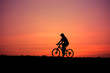 Silhouette of a man rides a bike at sunset