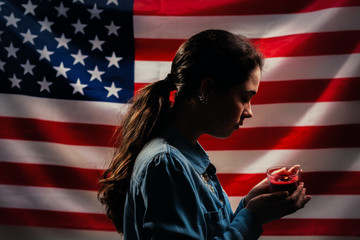 Memorial day. A woman holds a candle in memory of the victims. In the background, the American flag. Side view. Concept of American holidays