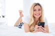 © deagreez - Closeup photo of cheerful beautiful house wife lady hold telephone writing blog post lying cosy bed freelancer quarantine white linen warm sunny morning stay home wear pajama room indoors