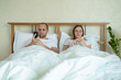 © Grustock - Couple lying in bed using mobile phone while ignoring each other. Man and woman addicted to smartphone social networks technology.